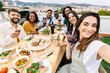 © Xavier Lorenzo - Diverse friends celebrating friendship and lifestyle on a summer terrace, sharing a dinner with wine and taking a group selfie during a festive gathering