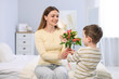 © New Africa - Little boy greeting his mom with flowers on bed at home