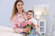 © New Africa - Little boy greeting his mom with flowers at home