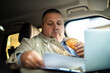 © Marko Geber - Businessman eating breakfast while working on laptop in parked car