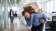 © ABAStock - A stressed businessman carrying a heavy stack of paperwork through a busy modern office