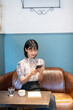 © amanaimages - カフェでスマホを見ながらくつろいでいる女性