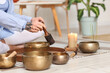 © Pixel-Shot - Young woman using Tibetan singing bowls on floor at home, closeup