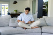 © Wavebreak Media - Asian man writing in spiral notebook with pen on gray sofa wearing blue-tee and headphones