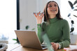 © Studio Marmellata - A young woman smiles while holding her phone to her ear, working on her laptop in a bright, modern office space.