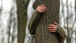 © shine.graphics - Person's hands embracing a tree trunk in a forest setting