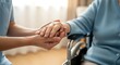 © Malin - Compassionate caregiver gently holds the hands of an elderly person seated in a mobility aid