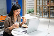 © Stella 16 - Beautiful Asian businesswoman eating breakfast in a cafe with a sandwich and coffee, and using laptop for work