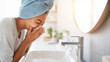 © Bonsales - Happy woman cleaning face with water splash from modern tap, enjoying freshness and daily hygiene routine for clear skin
