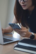 © tippapatt - Asian business woman busy working, using smartphone and laptop making a plan, writing in notebook. startup business. working remotely, close up, vertical