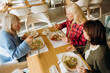 © m-art - Three friends share laughter and delicious food around a wooden table in a cozy cafe. Colorful salads and vibrant dishes delight as they savor the moment in good company.