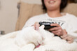 © hakase420 - ゲームをする飼い主の膝の上で毛繕いをする猫
