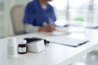 © STBSTD - Blurred healthcare professional writing patient notes on desk with medication bottles medical office clinic setting