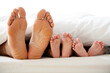 © designer rofiqul - Family feet of different sizes peeking out from under white duvet in bed toes soles