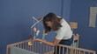 © Krakenimages.com - Woman bends over and adjusts hanging baby mobile above wooden crib in blue nursery building; tenderness bonding care.