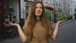 © Krakenimages.com - Woman shrugs her hands with palms up while wearing a brown dress on a narrow city street; uncertainty.