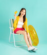 © sitthiphong - Happy smiling young Asian woman sit in deckchair and rubber ring in yellow color with holding credit card on blue background
