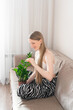 © Maria A - Woman wiping green plant with cloth while sitting on couch at home