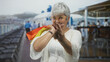 © Krakenimages.com - Woman holding colorful shopping bags over her shoulder, winking and making a finger heart gesture toward camera on street with deckchairs; playful joy.