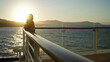 © Krakenimages.com - Woman resting bare hands on cruise ship railing on deck while leaning and looking toward horizon with sunset glare over ocean; serenity.