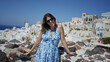 © Krakenimages.com - Woman holding sunglasses by her forehead, tilting head back on building ledge overlooking greek island town santorini; serenity.