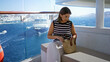 © Krakenimages.com - Woman holding sunglasses and straw bag seated on a terrace bench on a cruise ship building with ocean view; quiet relaxation.
