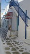 © Krakenimages.com - Woman walking on a stone street in mykonos near white buildings with blue stairs and red balconies; serenity.