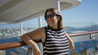 © Krakenimages.com - Woman leaning on railing with bare arms and head tilted up on building deck under bright sun; relaxation travel.