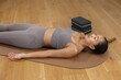 © 220 Selfmade studio - Calm peaceful young woman relaxing on mat doing yoga resting in corpse pose with closed eyes wearing gray activewear on wooden floor feeling deeply relaxed and mindful for physical wellness