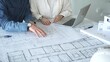 © volha_r - Two architects collaborate over blueprints and a model, using a compass and laptop to measure and plan detailed floor plans, symbolizing teamwork in property development