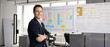 © fizkes - Modern planning culture. Happy confident male business professional project leader agile coach pose in office near sticky note roadmap strategy canvas look at camera. Wide image for horizontal banner