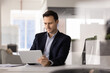 © fizkes - Focused adult Hispanic businessman reviewing digital and paper documents reading online report browsing web for information comparing data planning project using tablet pc at office desk. Copy space