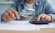 © Generative AI - Person Examining Documents with Magnifying Glass While Using Calculator for Financial Analysis