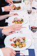 © Francis - Elegant formal dinner party with guests enjoying a gourmet meal of roasted meat, potatoes, and red wine. Sophisticated restaurant setting with white tablecloths and fine glassware for celebration.