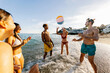 © Xavier Lorenzo - Diverse young friends laughing and playing a beach ball in shallow ocean water, splashing and enjoying sun-filled summer vacation vibes and carefree seaside fun together