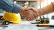 © farhan - Construction professionals shaking hands over blueprints and hard hat.