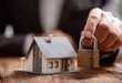 © Usman - Securing Your Home - A Hand Holds a Padlock Near a Miniature House Model.