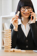 © sofiko14 - A smiling woman in a suit talks on her phone while holding wooden block , with a tower of blocks in the foreground