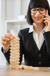 © sofiko14 - A smiling woman in a suit plays with wooden blocks while talking on her phone, demonstrating focus and multitasking