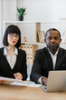 © sofiko14 - A focused African American man and a professional woman collaborate at a desk with a laptop and documents