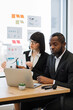 © sofiko14 - A woman in glasses explains a graph to an African American man during a business meeting, with a laptop and charts on the table
