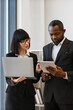 © sofiko14 - A professional woman and an African American man collaborate using a laptop and tablet in an office setting