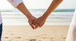 © Phlegmatic Tigress - Couple holding hands on a sandy beach with gentle waves and a clear sky in the background, showcasing a romantic moment by the sea