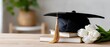 © lililia - A graduation cap sits on a flat surface with colorful flowers arranged around it on a simple background, offering space for text