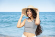 © Dulúapics - Happy young woman holding a sun hat while posing by the sea
