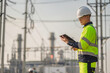 © reewungjunerr - Asian male electrical engineer holding digital tablet standing at power plant station. Professional energy industry technician working on infrastructure maintenance and renewable resource project.