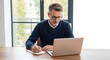 © FERDOUSI - Man working on a laptop while taking notes by hand on a wooden desk