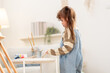 © Ekkasit A Siam - Asian preschool girl mixing paint on palette, kids art lesson at home, creative playtime in living room, easel canvas setup, fine motor skill practice, calm weekend learning moment, sunlit indoors