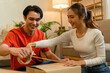 © MIND AND I - Young Asian Couple Packing and Sealing Cardboard Box Together at Home