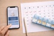 © Pavel - smartphone medication reminder beside calendar and weekly pill organizer